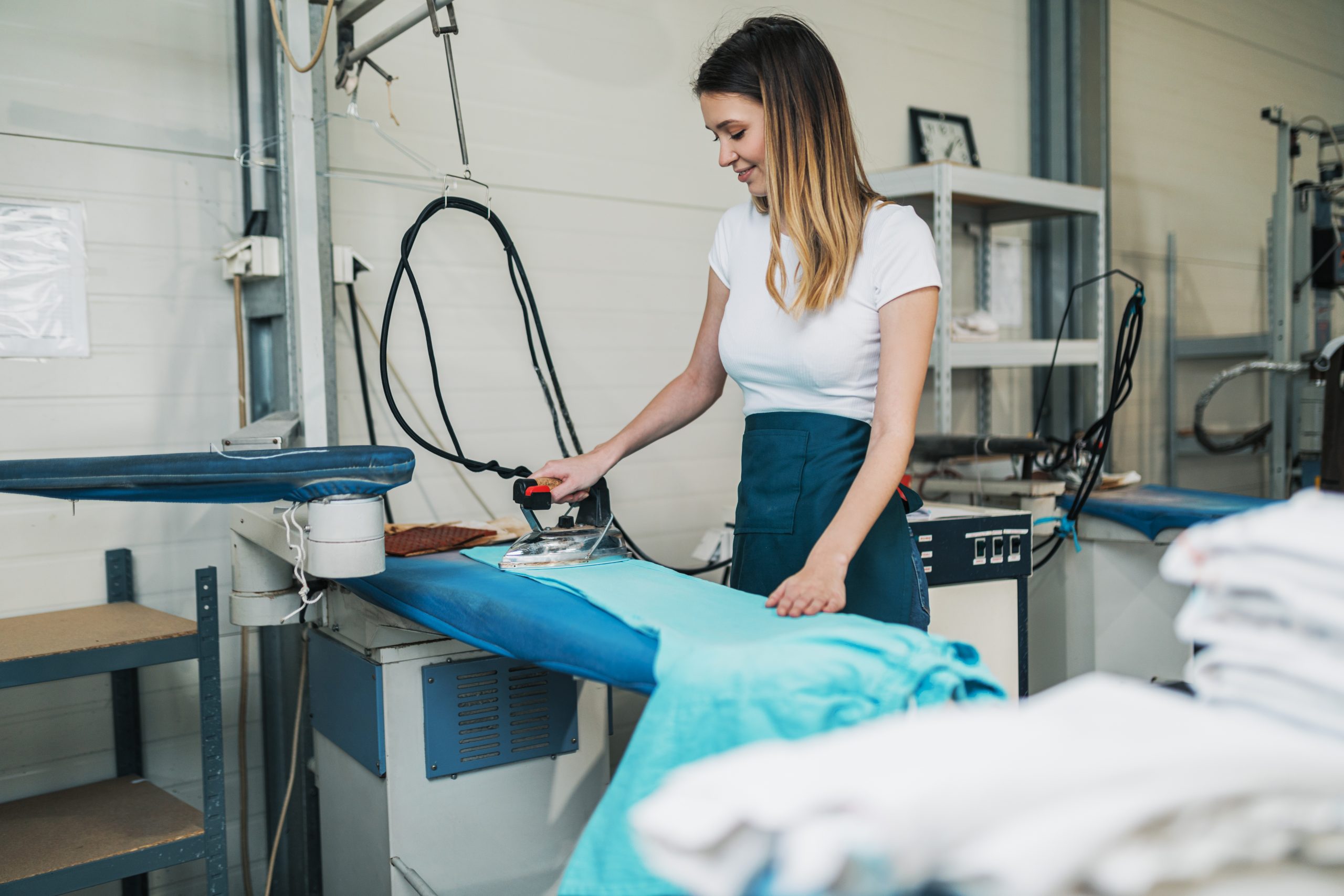Woman with iron working at ironing shop. Cleaning services.